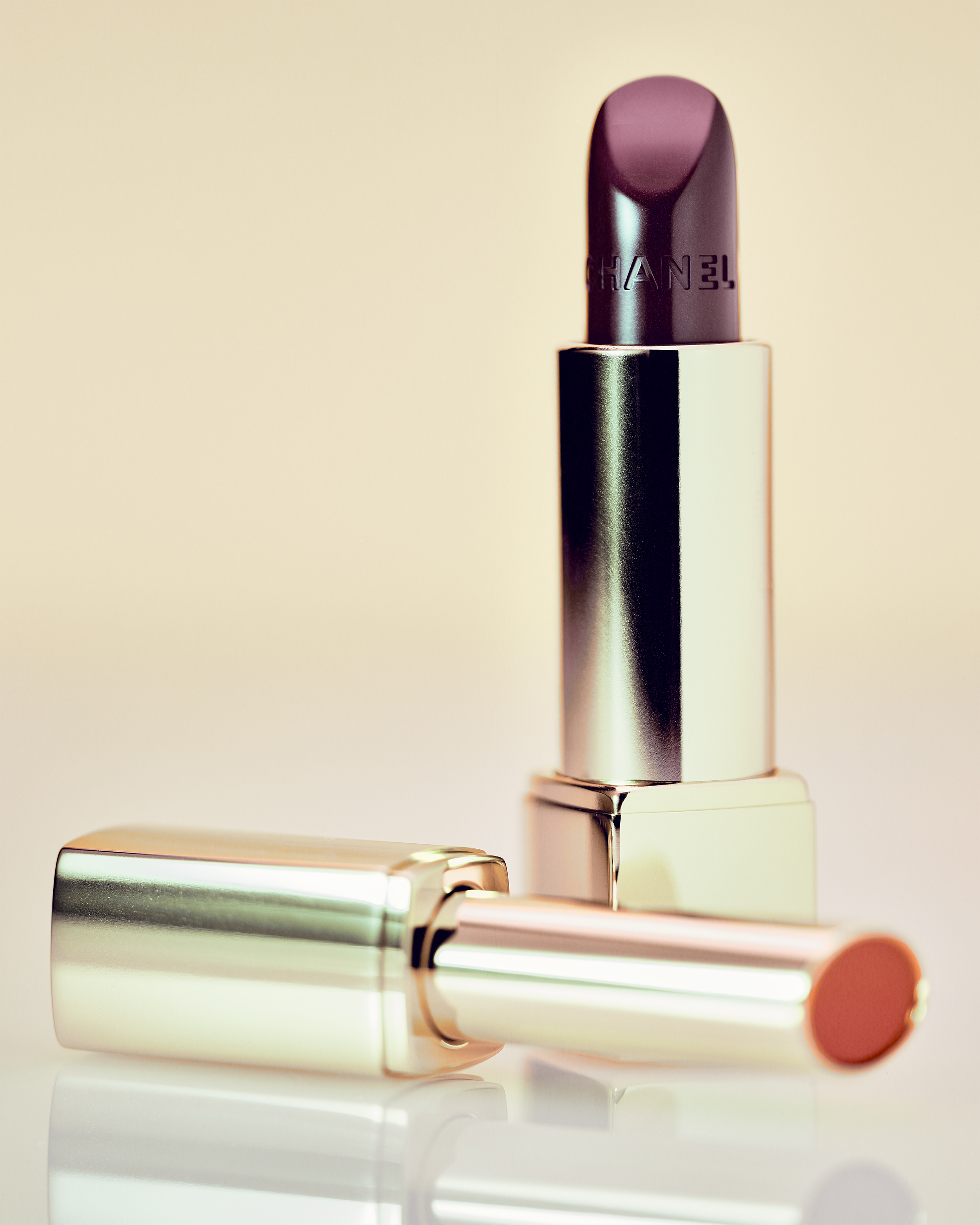 Still life photograph of two luxury lipsticks in soft lighting, one standing upright and the other lying down. 