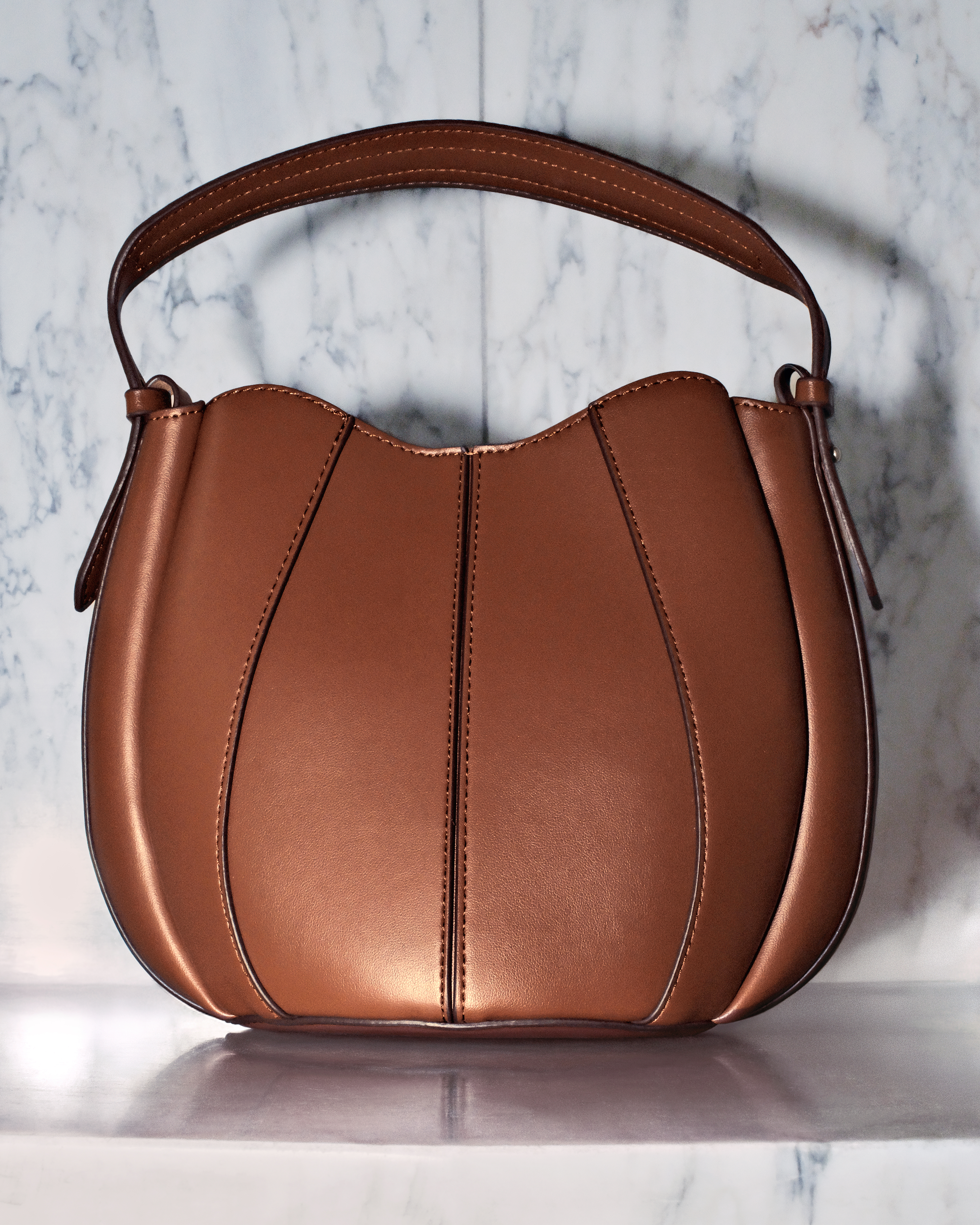 Zara handbag held by a model, shown in profile against an elegant Parisian flat entrance with marble walls. 