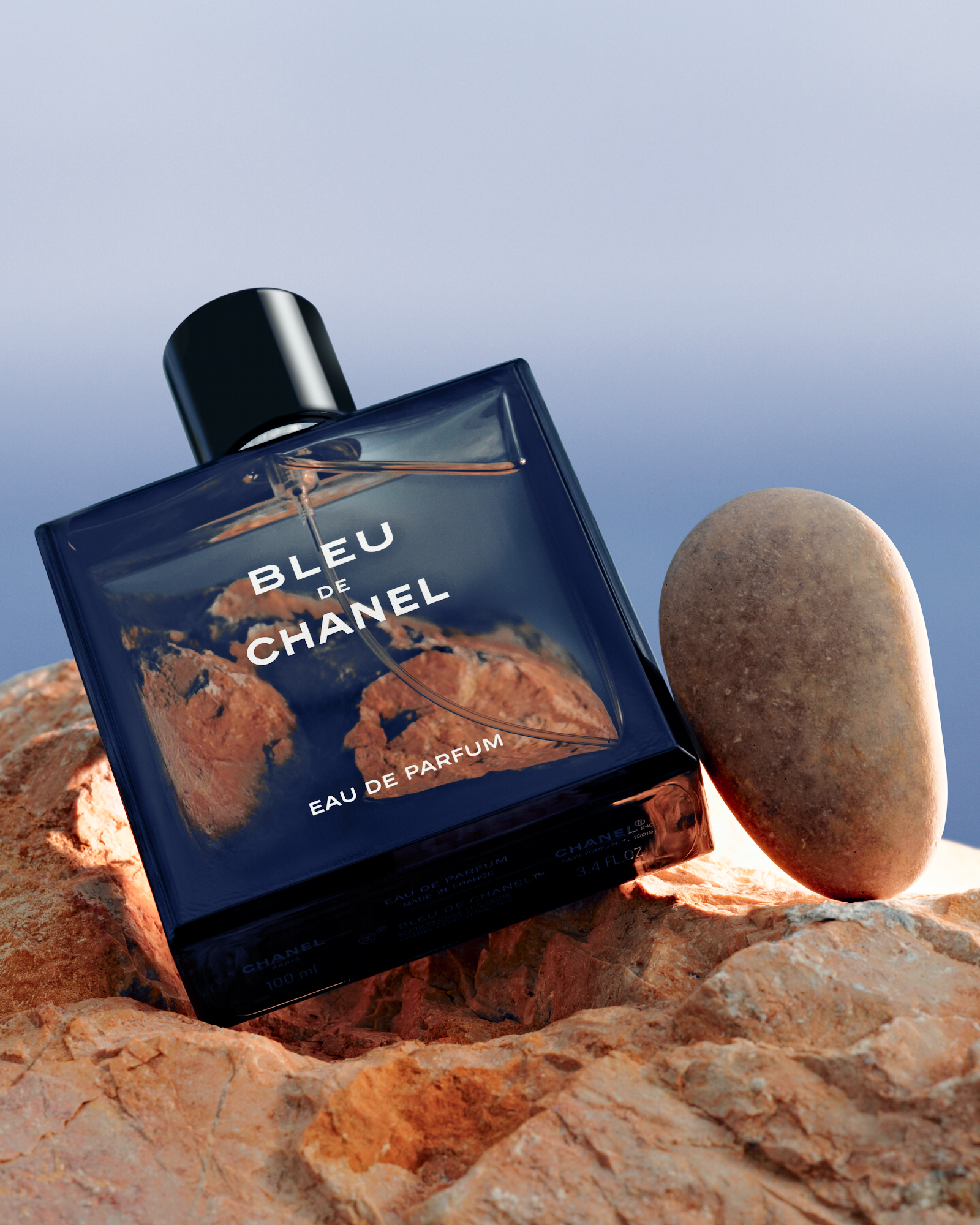 Chanel Bleu cologne bottle placed on a coastal rock with a round stone. 