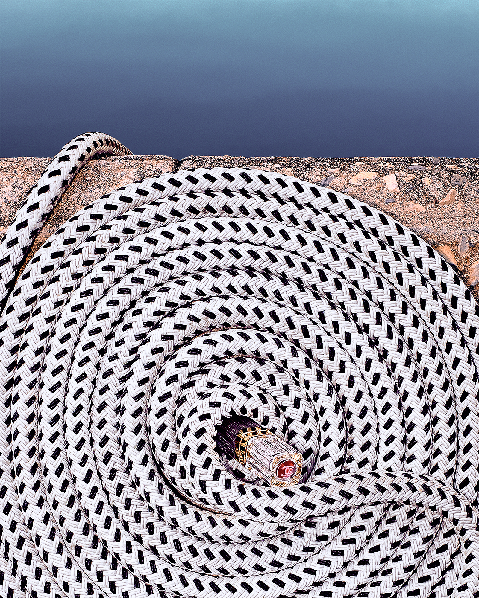 Chanel lipstick placed in the center of coiled white rope on a beach. 